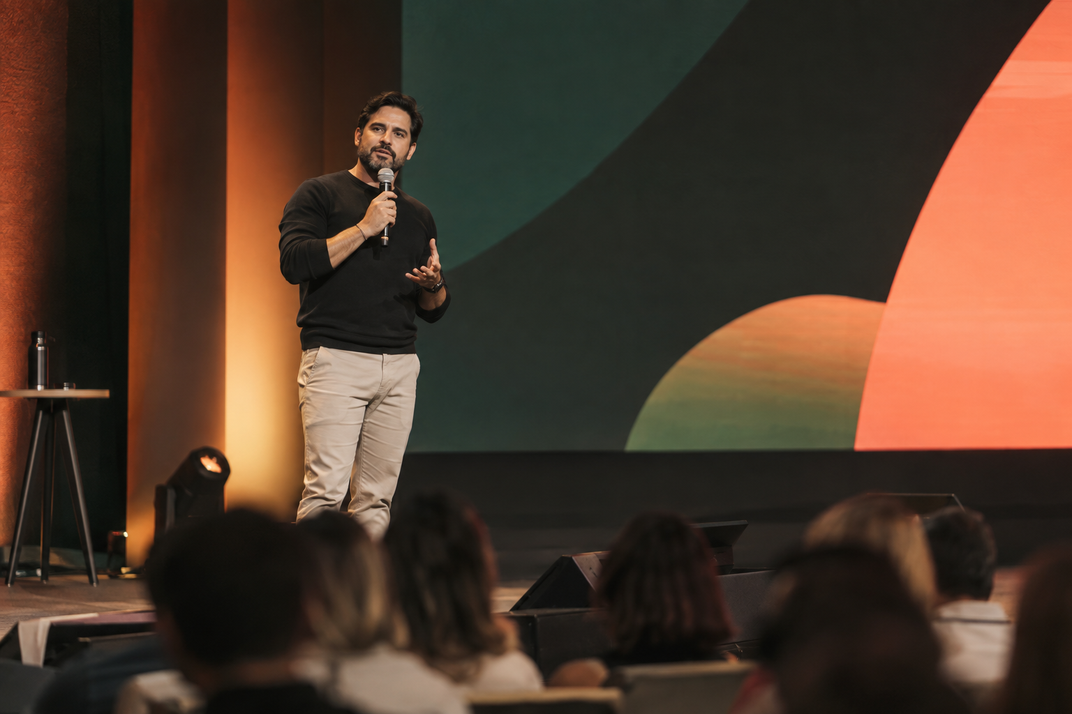 Infoprodutor fictício apresenta no palco diante de uma plateia em um evento de negócios digitais.